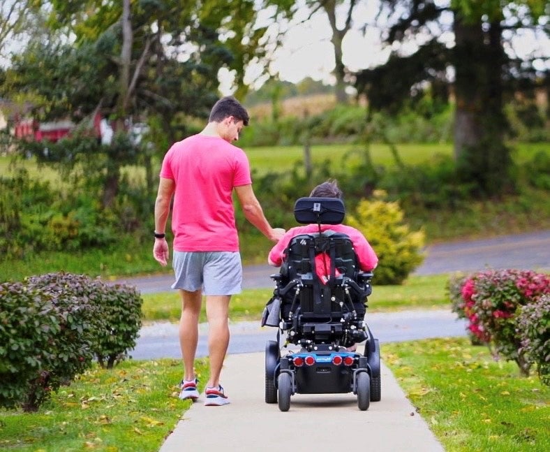 Luke walking beside Elliott, in his wheelchair